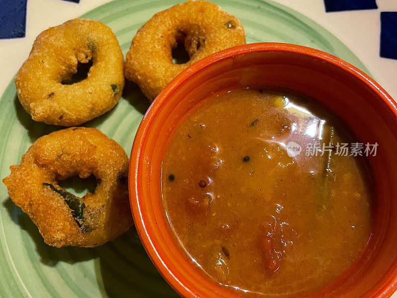 全帧图像的图案盘子包含一个早餐零食自制的Medu vada(软油饼)和一碗桑巴(辣扁豆和蔬菜炖)，用Vigna mungo(黑扁豆)做的美味甜甜圈，高架视图